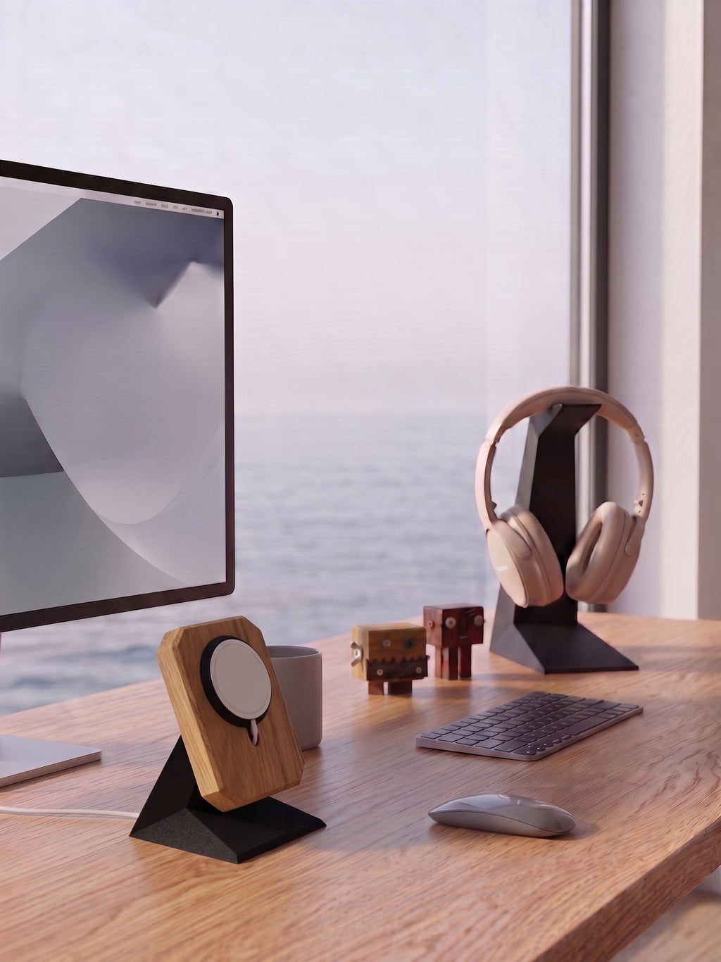 KI-generiertes Bild: Ein heller, aufgeräumter Arbeitsplatz an einem Holztisch mit Blick auf das Meer durch ein großes Fenster. Rechts steht ein Computerbildschirm mit einem Holz-MagSafe-Ladeständer davor und einer Kaffeetasse daneben. Auf dem Tisch liegen eine graue flache Tastatur und eine passende Maus. Links befindet sich ein schwarzer Kopfhörerständer mit beigen Over-Ear-Kopfhörern, davor stehen zwei kleine, handgefertigte Holzroboter-Figuren.